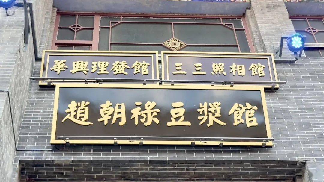 金街建筑立面上悬挂的老商号招牌，黑底金字书写"华兴理发馆""三三照相馆""赵朝禄豆浆馆"等。