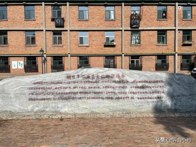钢32街坊入口处的花岗岩刻石，刻有"钢三二街坊历史文化街区简介"全文。身后红砖楼即为社区党群服务中心所在地。