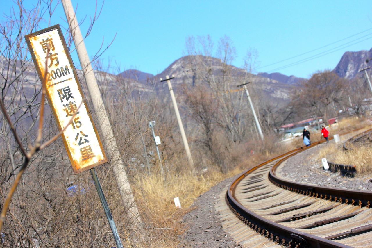 包石铁路沿河谷蜿蜒前行，轨道在干旱的山谷中穿行。沿线的速度限制牌和锈蚀的铁轨说明这条线已经停运。