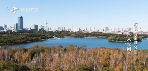 从南湖公园上空俯瞰，湖面开阔，秋色中的公园与远处城市天际线相接