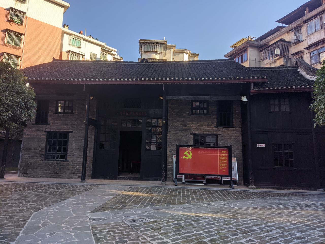 八路军驻湘通讯处旧址外景，青瓦白墙的二进砖木建筑，背景可见现代高层住宅