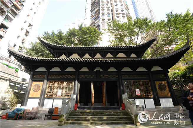 修缮后的东华观藏经楼，黑色木柱、白色墙体、重檐歇山屋顶在周边高楼包围中显现