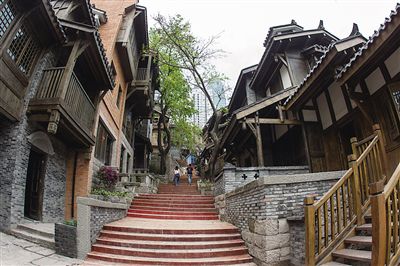 改造后的十八梯主梯道日景，青灰色仿古建筑沿石阶排列，远处可见解放碑商圈的摩天楼