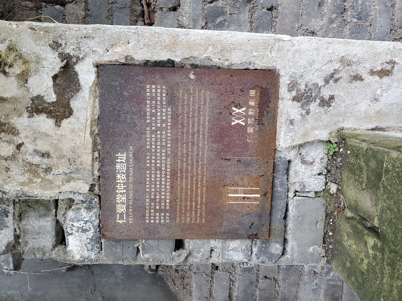 生锈的仁爱堂信息牌嵌在砖墙上，介绍建筑历史