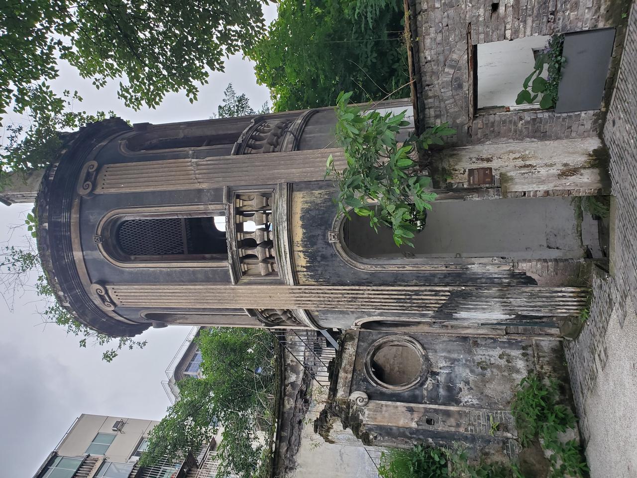 仁爱堂圆形钟楼矗立在崖顶杂草中，罗马柱和拱形窗框仍清晰可见