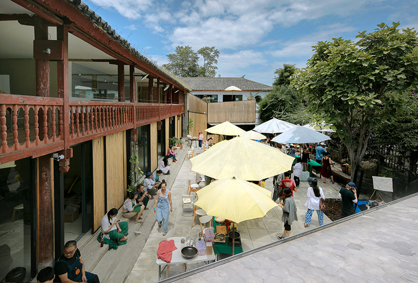 柴米多农场的户外用餐区和庭院，黄色遮阳伞下人们在用餐，背景是传统白族木结构建筑和竹林