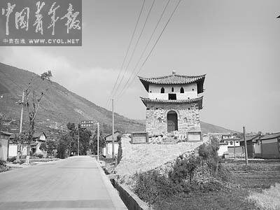 A traditional Chinese watchtower with a tiled roof stands on a raised stone foundation next to a rur