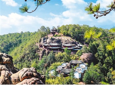 A lush green hillside features ancient cave temples and pavilions, with traditional Chinese architec