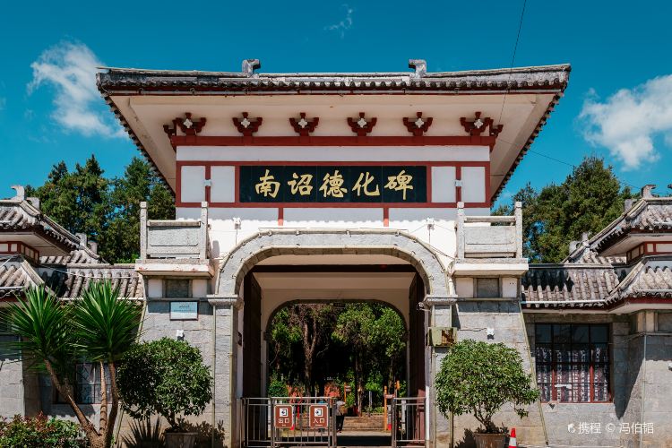 A traditional Chinese entrance gate with a sign inscribed with Chinese characters, flanked by greene