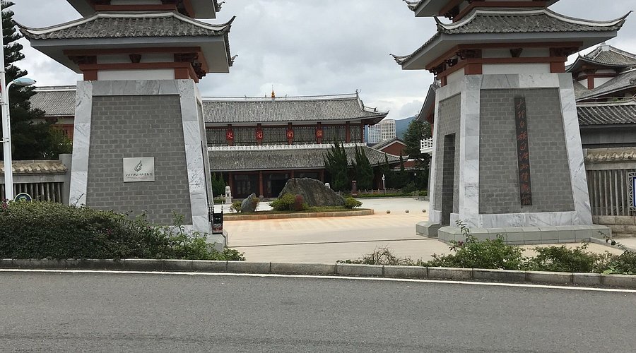 A traditional Chinese building complex with ornate rooftops is visible behind two stone gate pillars