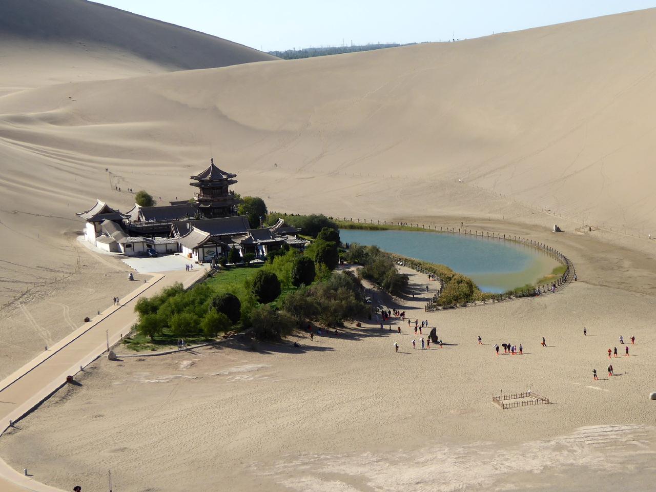 从鸣沙山沙丘顶北望:前景沙丘、中景月牙泉、远景绿洲边界和敦煌市区天际线