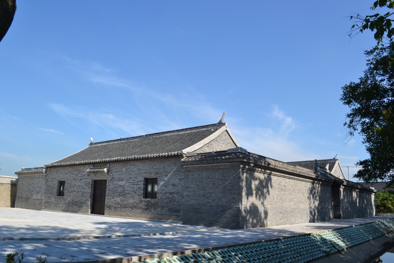 A reconstructed traditional Chinese building with grey brick walls and curved rooflines, set against a bright blue sky, 