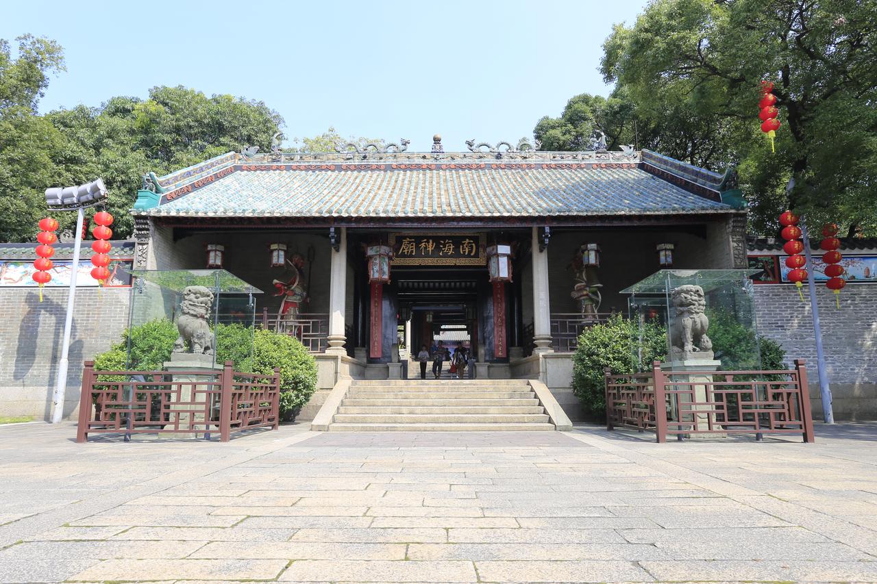 A traditional Chinese temple with intricate roof details, flanked by stone lions, stands amid greenery with red lanterns
