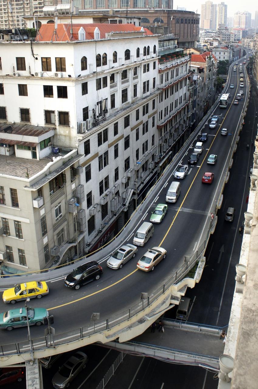 A busy elevated road runs alongside aging white buildings with numerous windows and air conditioning units, in a dense u