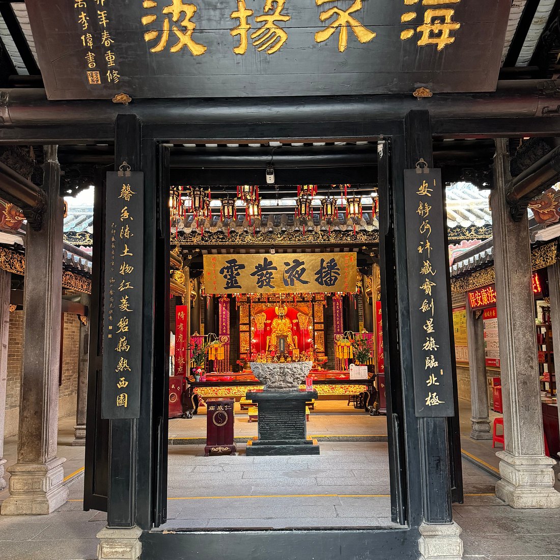 An ornate temple or shrine with a red and gold altar featuring a seated statue, decorated with hanging lanterns and trad