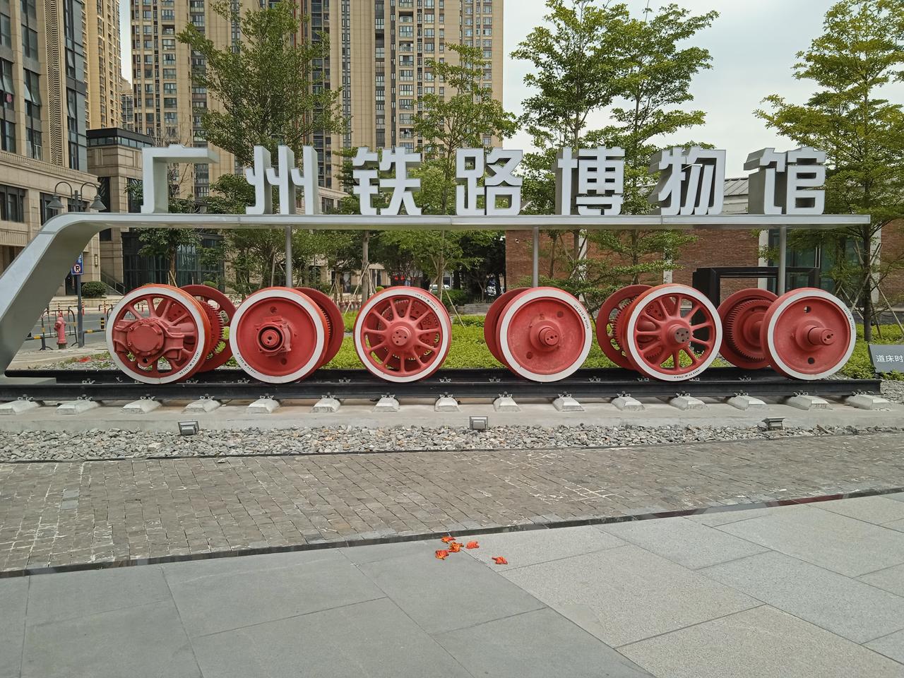 A train wheel display in front of buildings with a sign indicating the Guangzhou Railway Museum, symbolizing the transfo