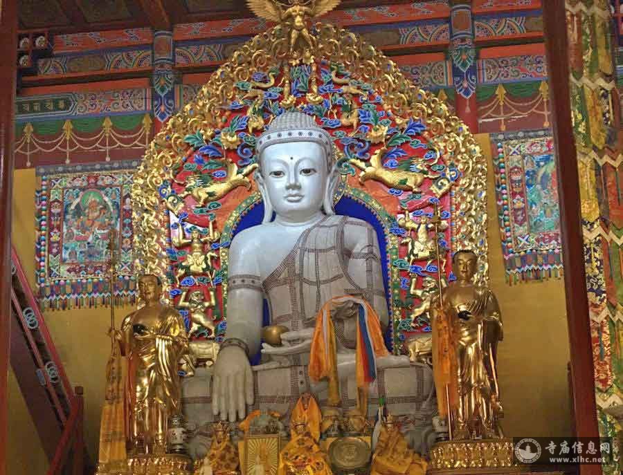 A large white Buddha statue is seated with a peaceful expression, surrounded by