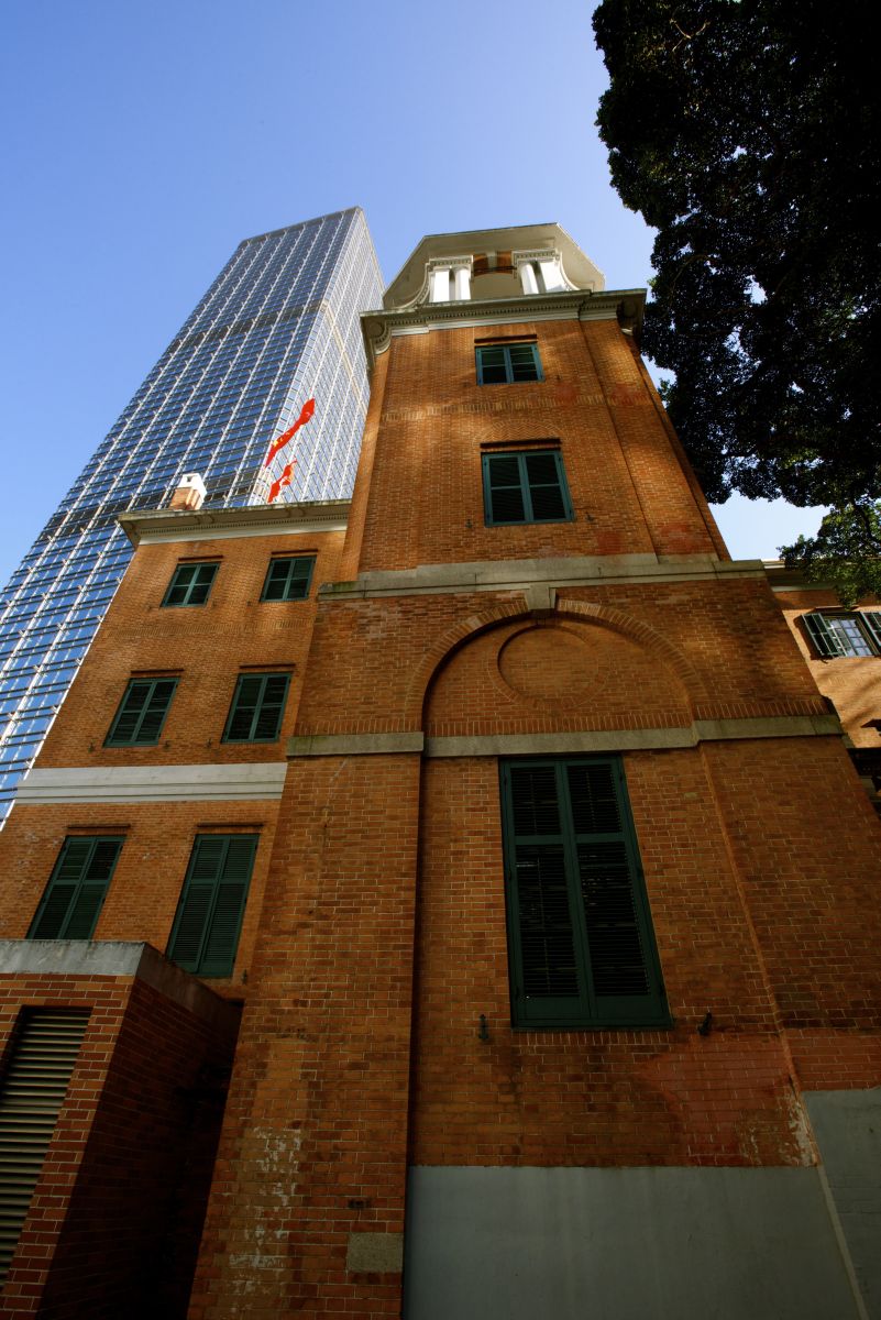 炮台里斜坡上仰望大楼北侧，左侧可见现代玻璃幕墙的长江集团中心，两栋建筑间隔仅一栋楼的距离。