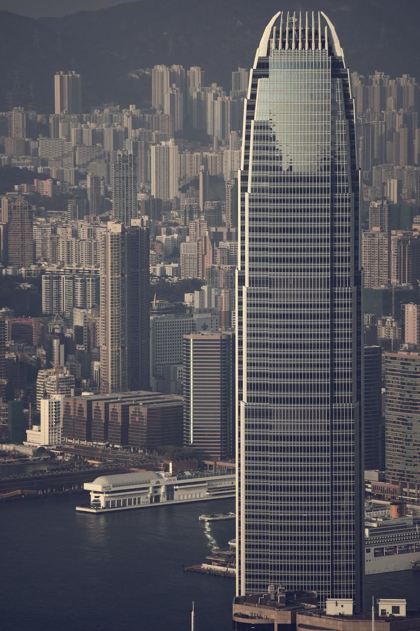 Two IFC 从地面仰视，银灰色幕墙和珍珠色竖框在蓝天下清晰可见，锥形轮廓从 57 米见方底座收窄至顶部 39 米。