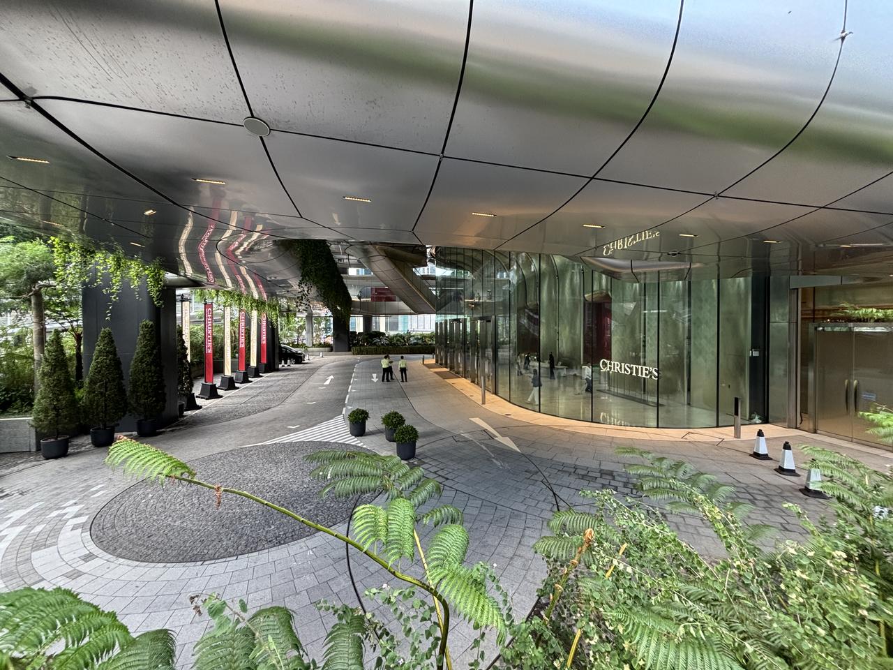 The Henderson地面层落客区，建筑的弧线造型从地面层就开始展现，后方可见中环核心区的高层建筑群。