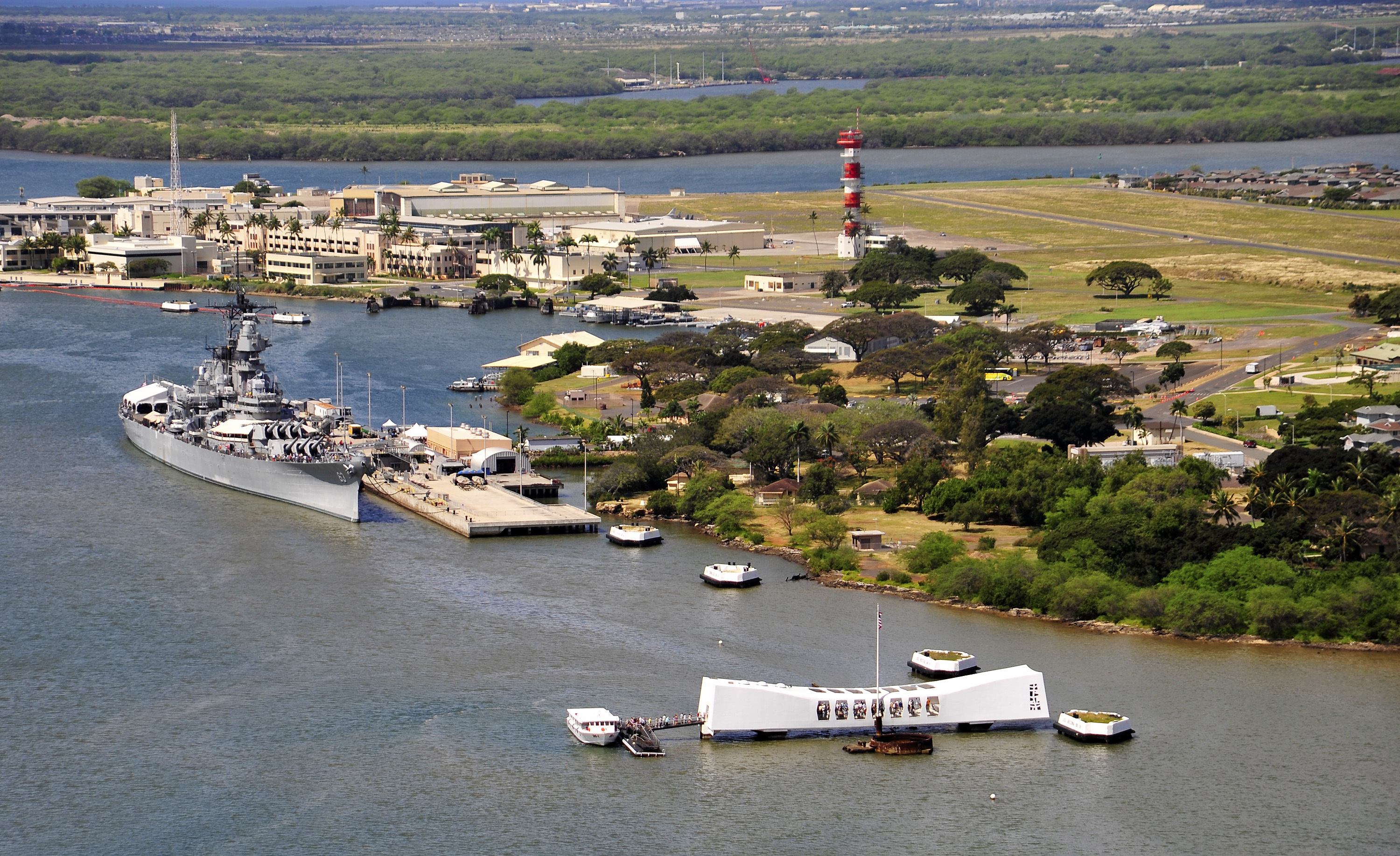 USS Missouri 和 USS Arizona Memorial 同框，两者隔着港湾水面相望，Ford Island Control Tower 在背景中