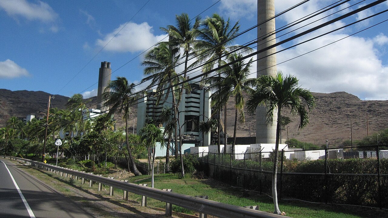 从 Farrington Highway 看 Kahe 发电站的主厂房、烟囱和储油罐，前方为公共道路和海岸线