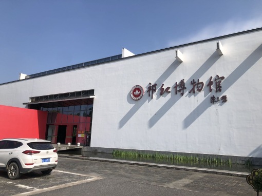 祁红博物馆入口区域：红色装饰墙与"祁红博物馆"标识，前方为景观水池和停车场