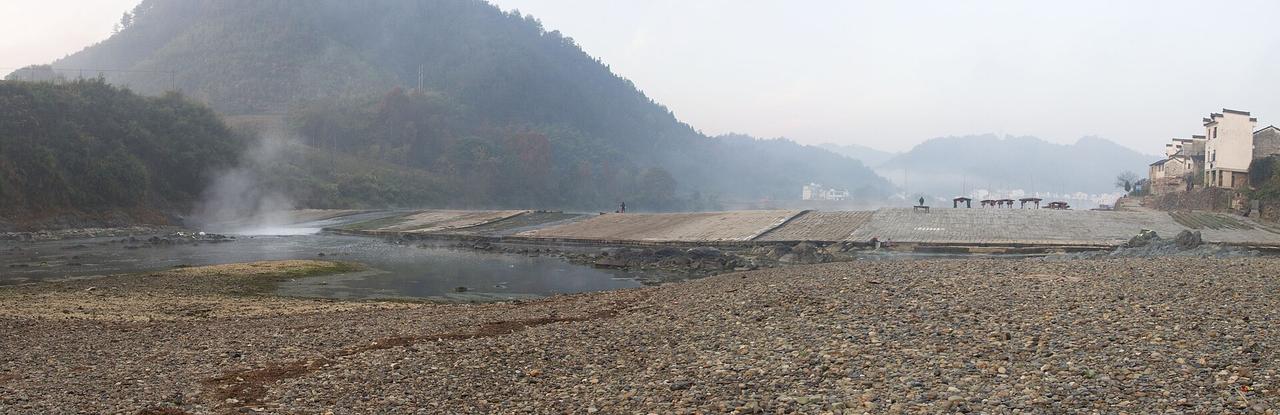 冬季清晨的渔梁坝全景，江水从坝顶平缓漫过，坝体花岗岩条石清晰可见