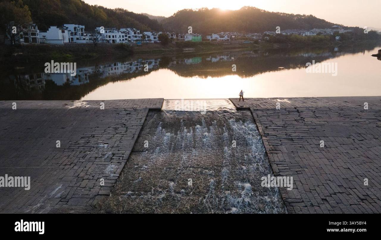 渔梁坝全景，水流漫过坝顶，岸边为渔梁村民居