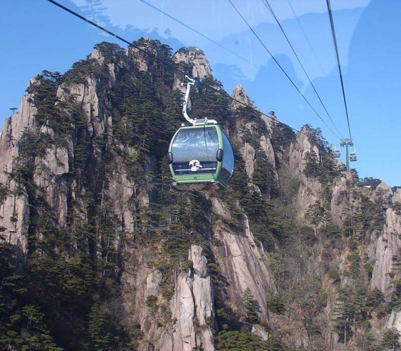 黄山云谷索道缆车悬于陡峭岩壁前，远处可见银杏树