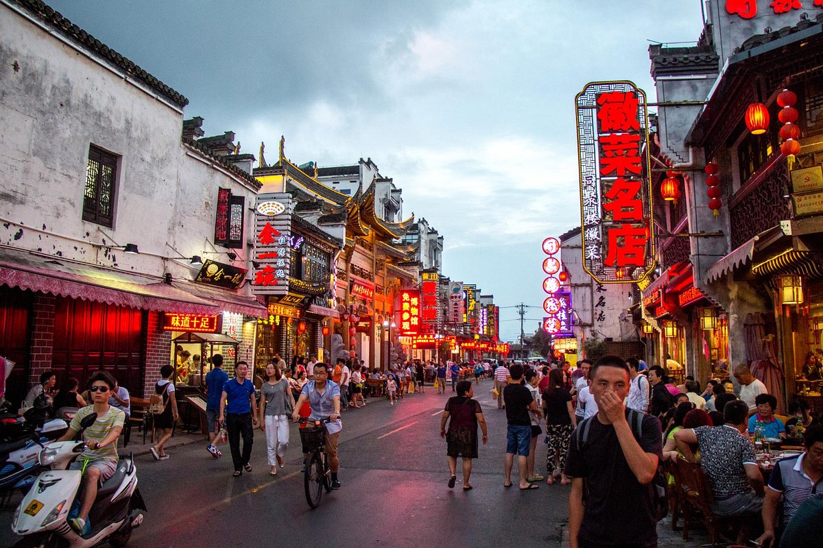 屯溪老街夜景，徽派建筑立面上红灯笼与霓虹招牌闪烁，街道上人流如织
