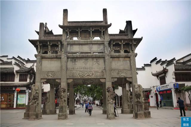 歙县许国石坊八脚跨街全景，石狮立于柱基，行人从下方穿行