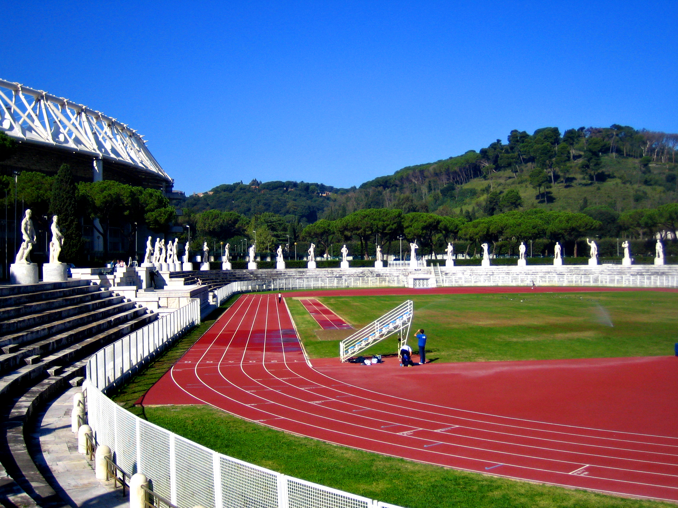 Stadio dei Marmi 全景，椭圆田径场外围白色大理石雕像圈，背后是 Stadio Olimpico