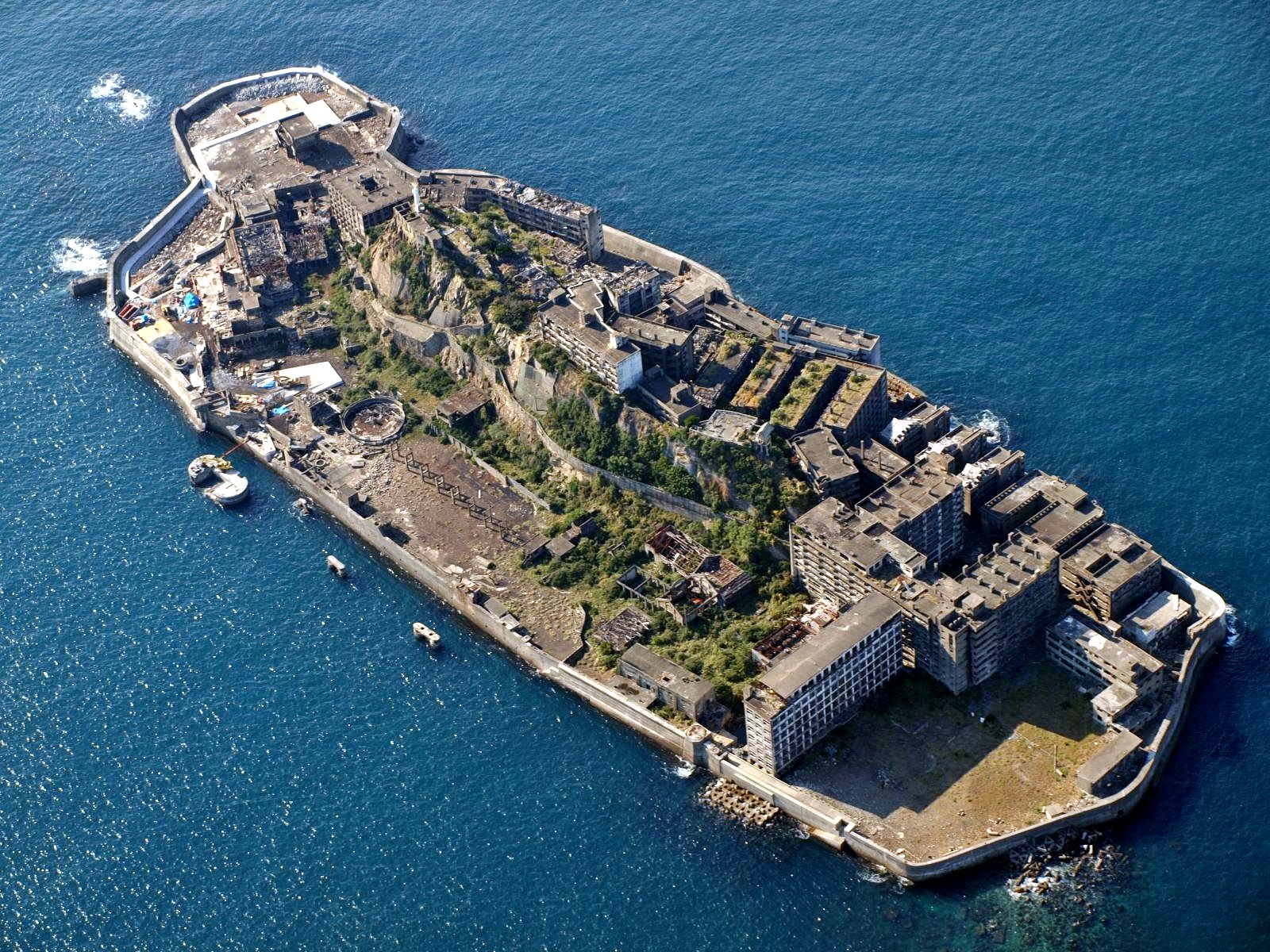 从侧角度看到的军舰岛，灰色废弃建筑和混凝土防波堤，周围是深蓝色海水