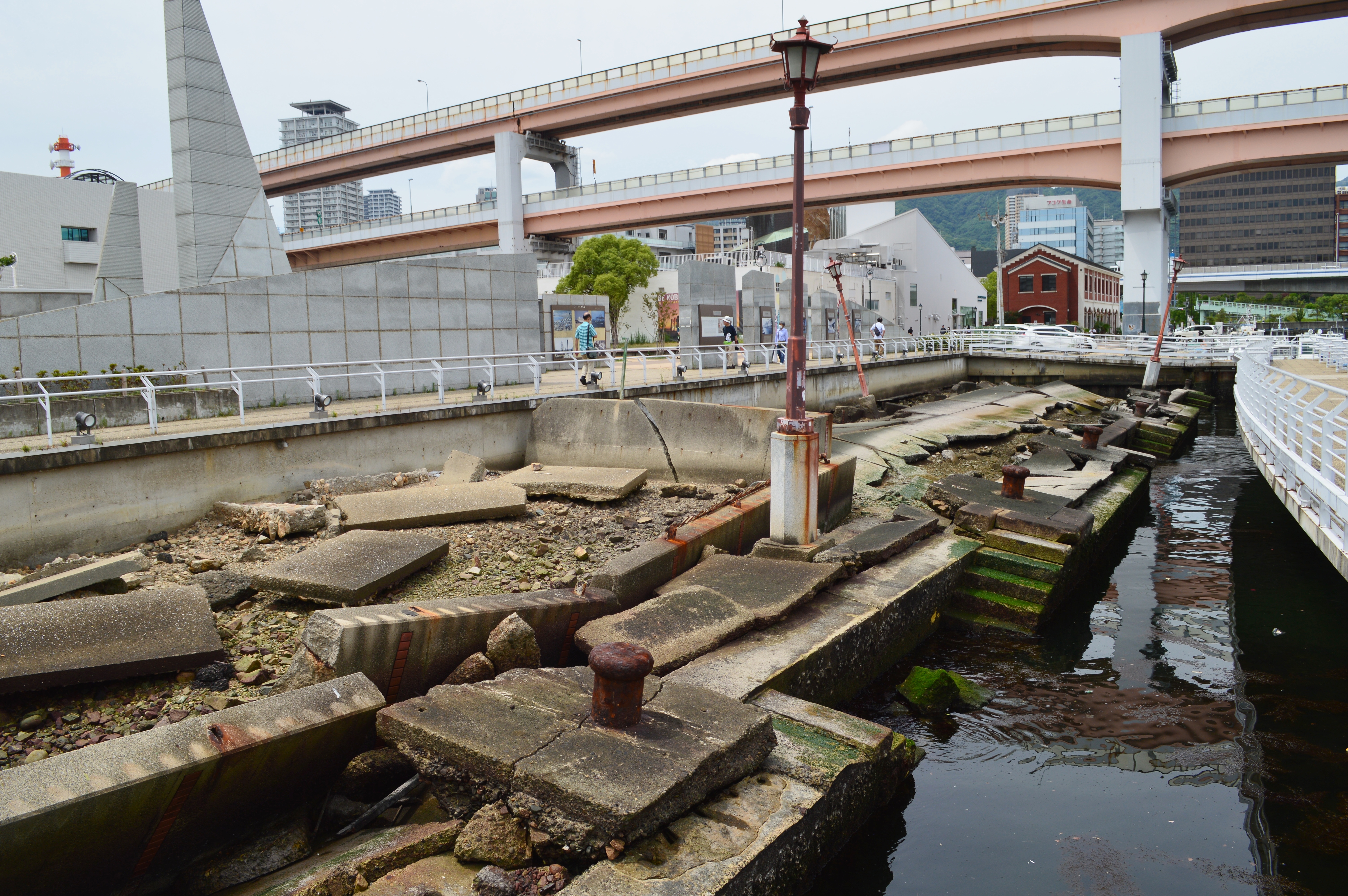 神户港震灾纪念公园被災岸壁全景，混凝土面板断裂、钢筋外露、路面起伏
