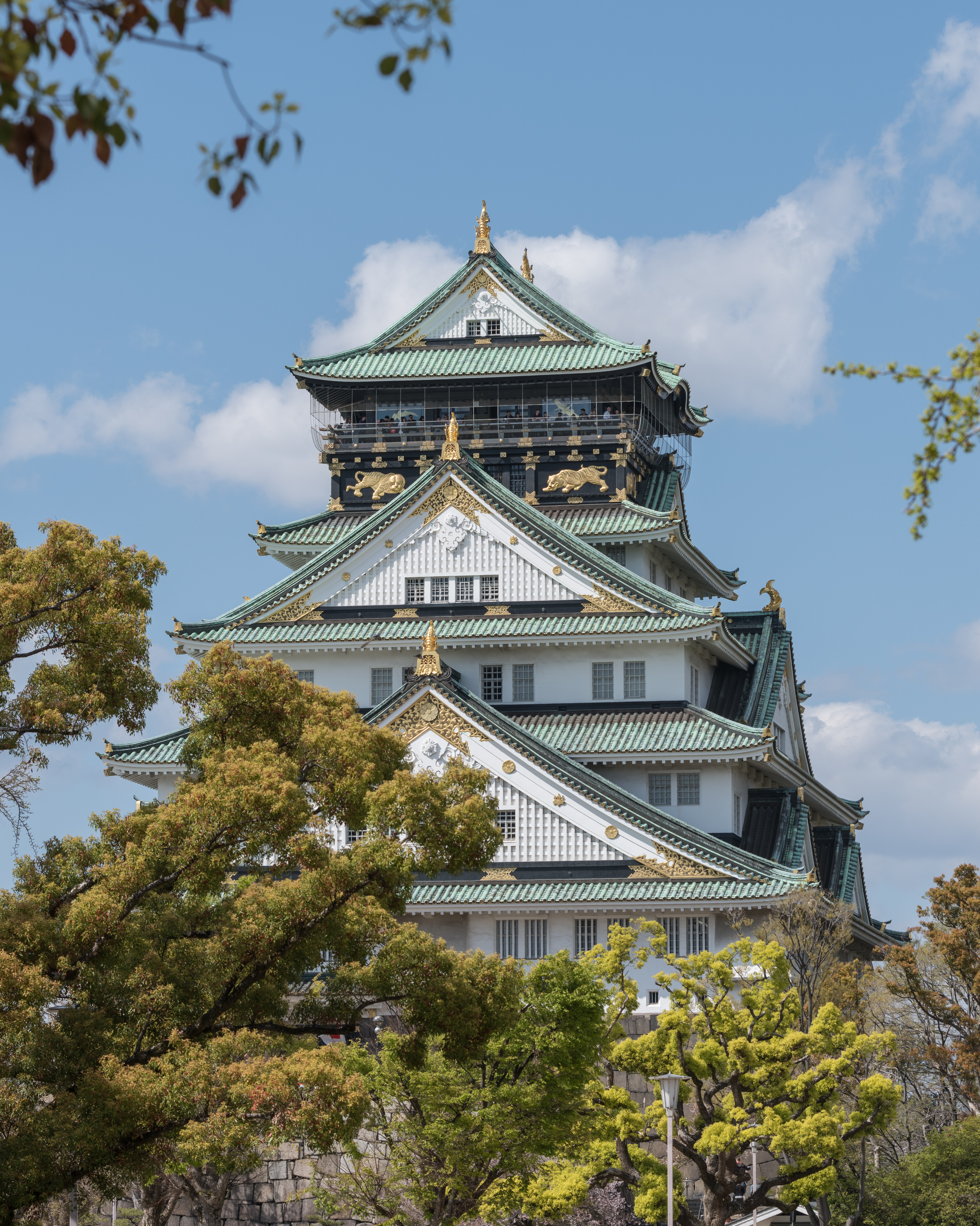 大阪城天守阁正面全景，白色外墙、绿色铜瓦屋顶、金色鯱装饰，坐落在德川时代的花岗岩石垣上
