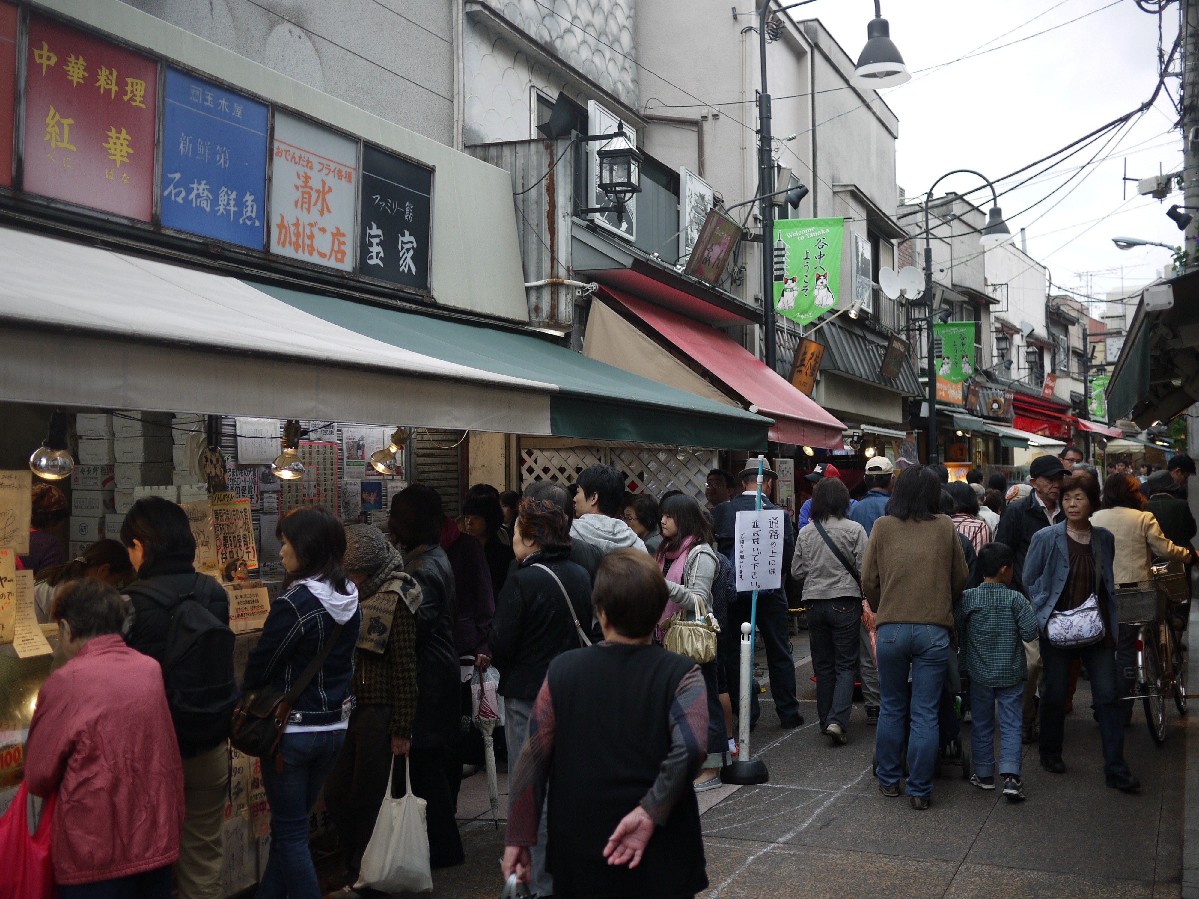 谷中银座商店街内部，两侧木造店铺屋檐低矮伸出，红色灯笼悬挂在店铺前沿