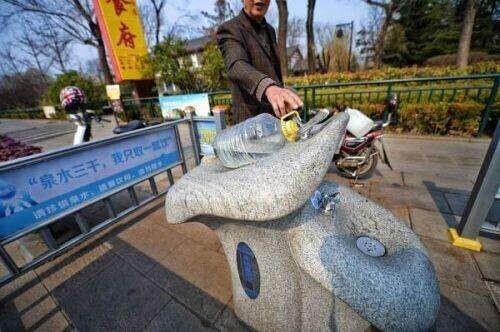泉城路沿线的石质荷花形泉水直饮台，市民正在按压取水