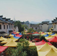 市集原址在雕塑瓷厂内的场景，彩色帐篷与老厂房建筑形成对照