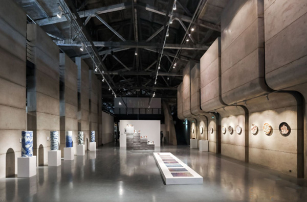 真如堂老厂房改造展厅内部,保留厂房钢桁架屋顶,标准化展柜陈列陶瓷茶器、花器和香具