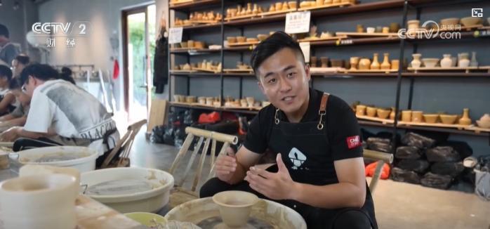 非遗传承人坐在拉坯机前演示拉坯，旁边有游客在观摩