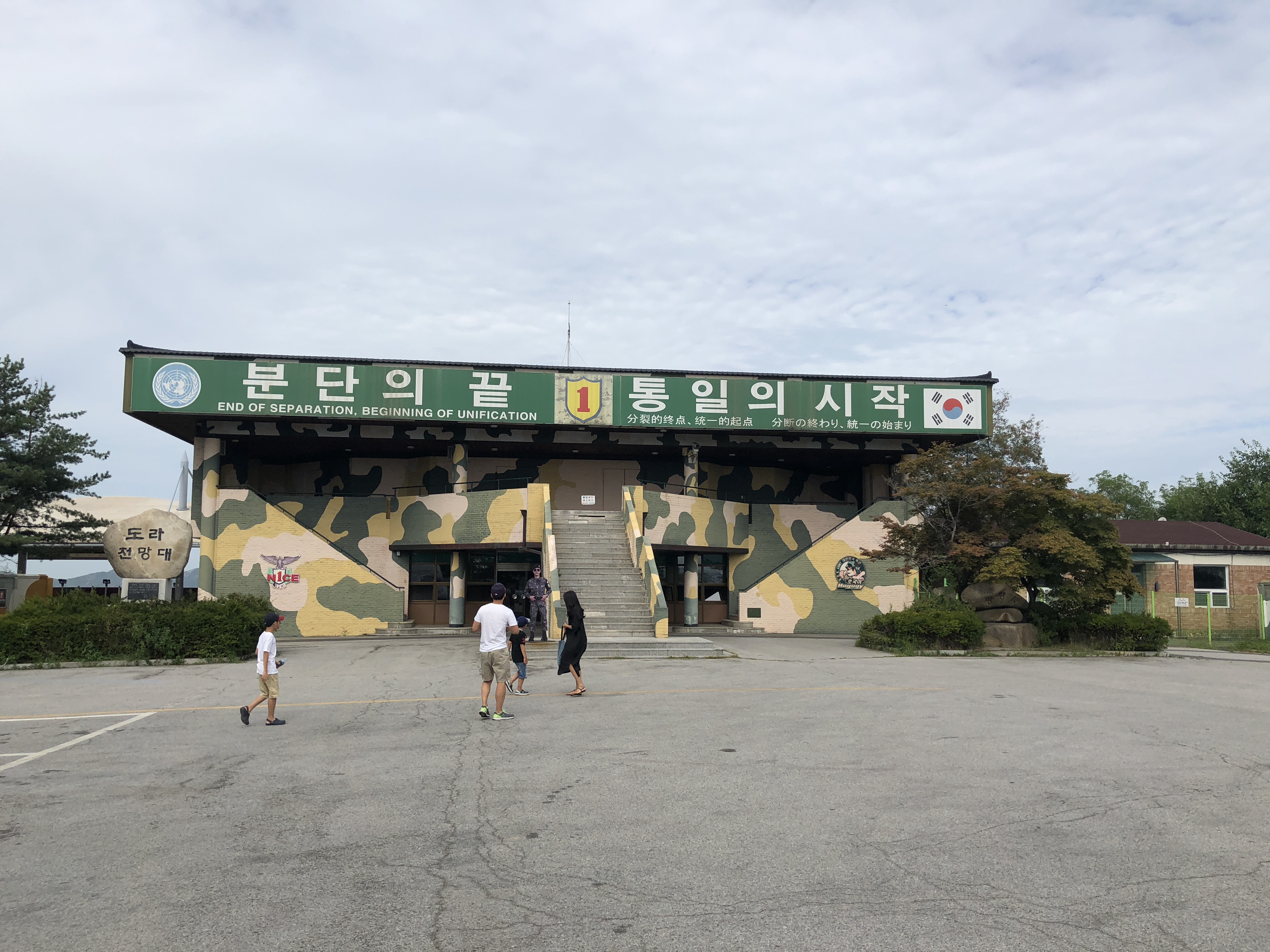 都罗展望台白色现代建筑，前方广场有DMZ标识牌，背后是群山
