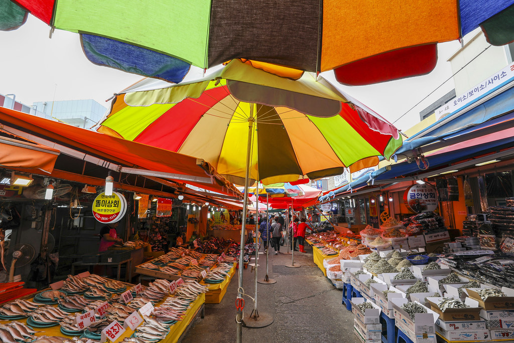 札嘎其市场户外街摊，彩色遮阳伞下排列着新鲜海产品的木箱摊