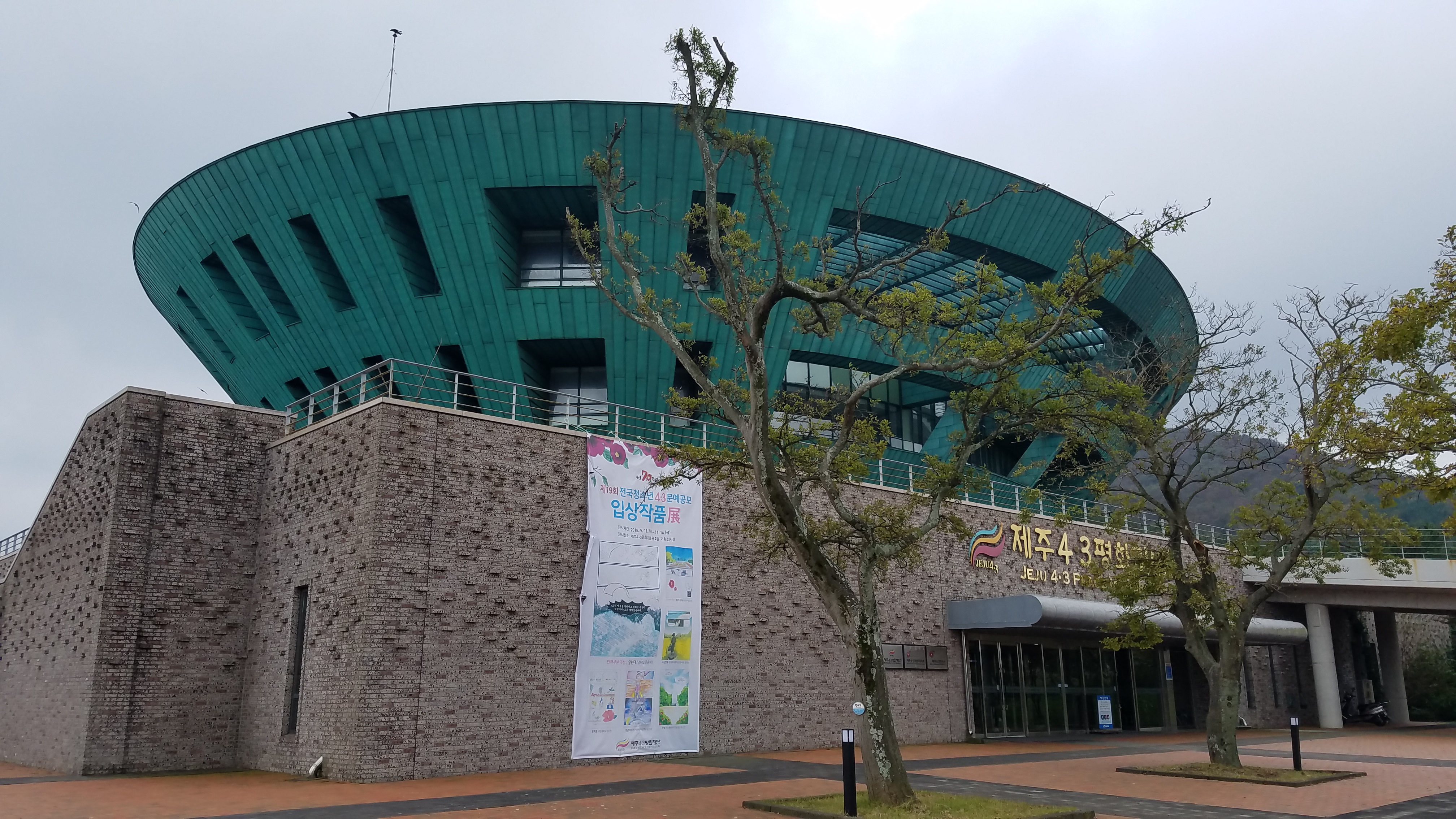 4·3 和平纪念馆外观，弧形玻璃幕墙的现代建筑，前方是开阔的追悼广场
