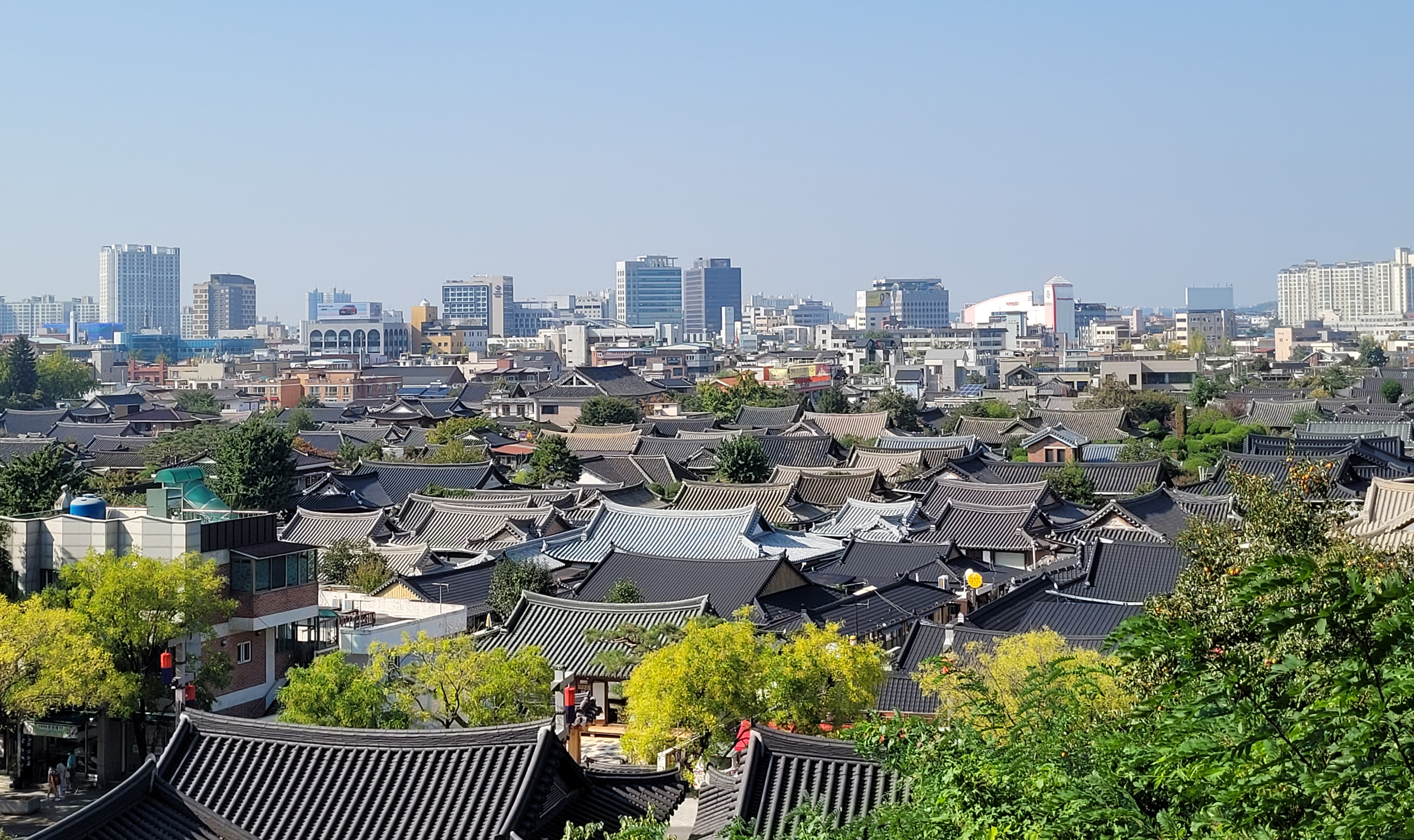 全州韩屋村鸟瞰，密集的灰色韩屋瓦屋顶连绵展开，远处可见现代城市