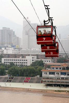 A red cable car with passengers numbered 7, 8, and 9 is suspended on a cable abo