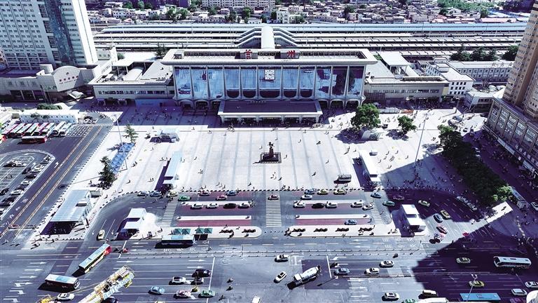 A large modern train station with a spacious plaza in front, featuring multiple 