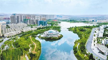 高楼林立的城市景观中，一座环绕着水域的现代建筑坐落在绿地中，显示出兰州新区的发展与宜居环境。