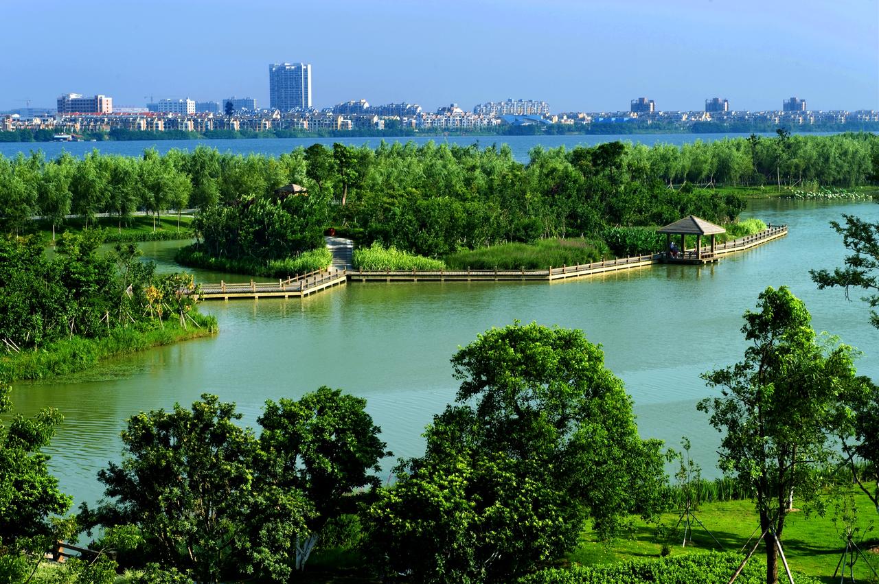 艾溪湖湿地公园鸟瞰，湖面开阔，远方可见高新区工厂建筑群