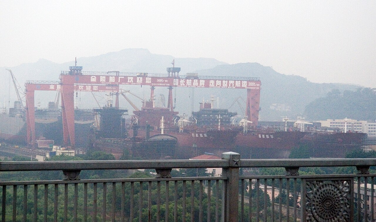 金陵船厂红色龙门吊临江矗立，背景是厂房和江岸